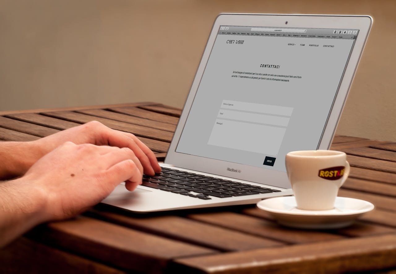 our-story Close-up of hands typing on a laptop next to a cup of coffee on a wooden desk.